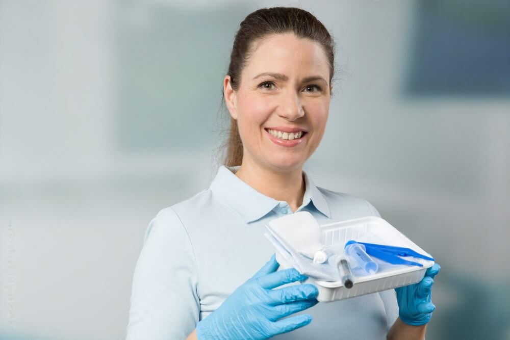 A friendly nurse with a catheter set in front of a clinic room