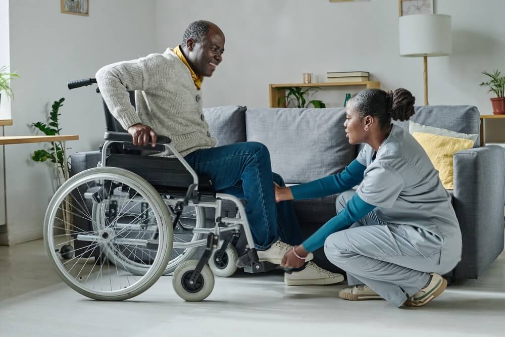 African young girl helping senior man with disability to sit on wheelchair