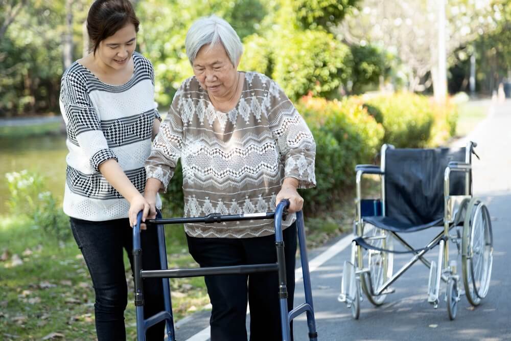 Asian adult woman or daughter support,helping senior mother to stand up from wheelchair,happy elderly patient use walker during