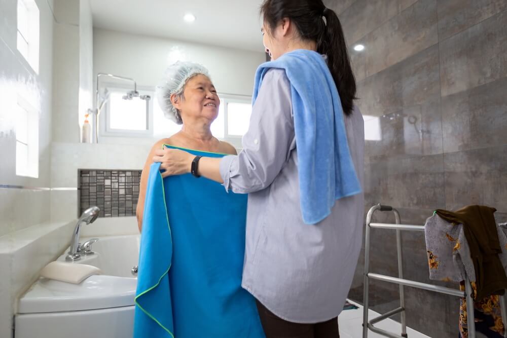 Asian female care assistant help her senior mother wipe her body after shower in bathroom at home