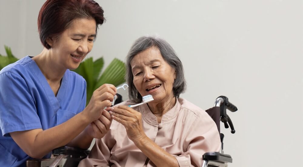 Caregiver take care asian elderly woman while brush teeth.